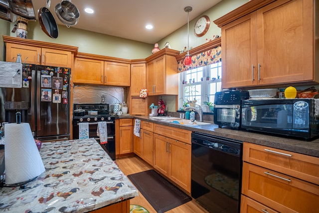 kitchen featuring decorative backsplash, light wood-style flooring, brown cabinets, black appliances, and a sink