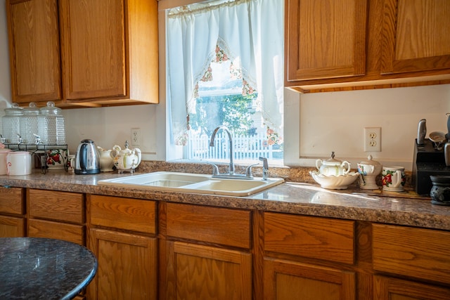 kitchen featuring decorative backsplash, dark stone countertops, a sink, and brown cabinets