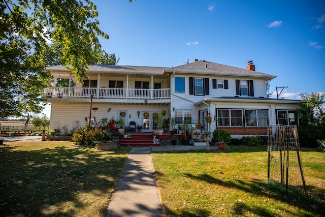 rear view of property featuring a balcony, a chimney, and a lawn