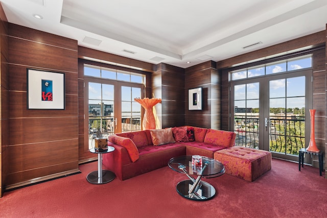 carpeted living room with french doors, wood walls, and a tray ceiling