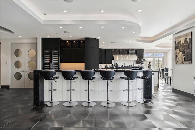 kitchen featuring a large island, a kitchen breakfast bar, a tray ceiling, and ventilation hood