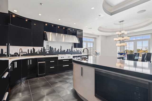 kitchen with dark tile patterned floors, a tray ceiling, sink, decorative light fixtures, and tasteful backsplash