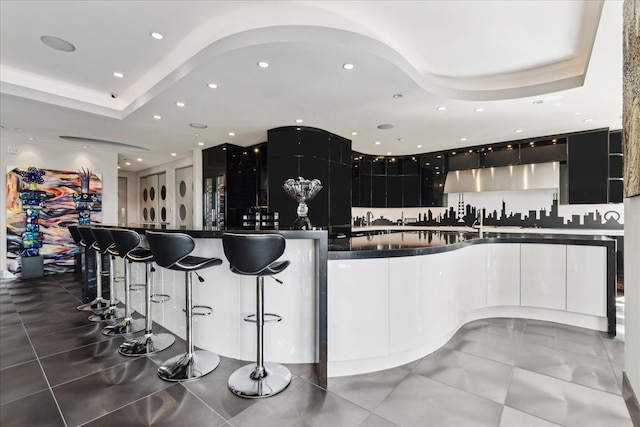 kitchen with a kitchen island with sink, dark tile patterned floors, and a raised ceiling