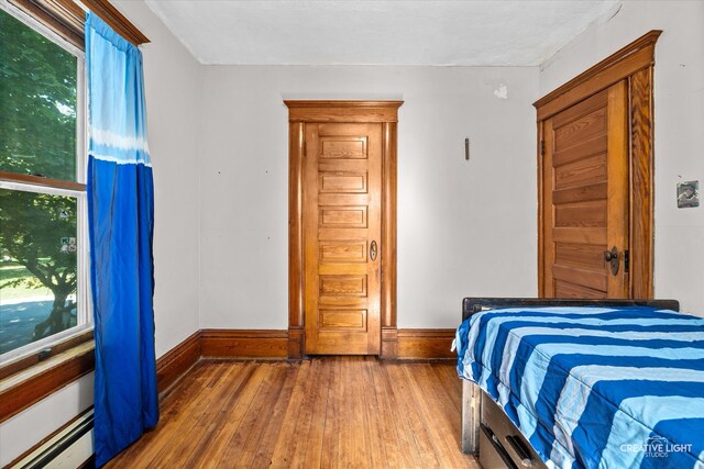 bedroom featuring baseboard heating, hardwood / wood-style floors, and multiple windows