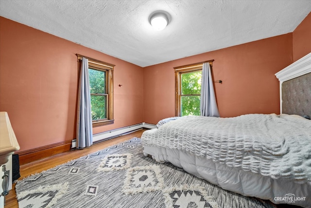 bedroom featuring wood-type flooring, a textured ceiling, a baseboard radiator, and multiple windows