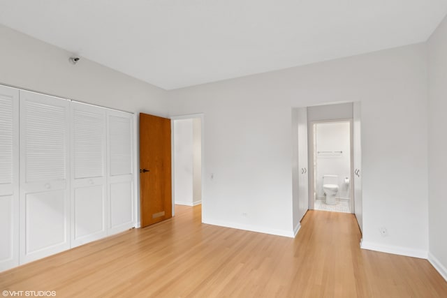 unfurnished bedroom with ensuite bathroom, a closet, and light hardwood / wood-style floors