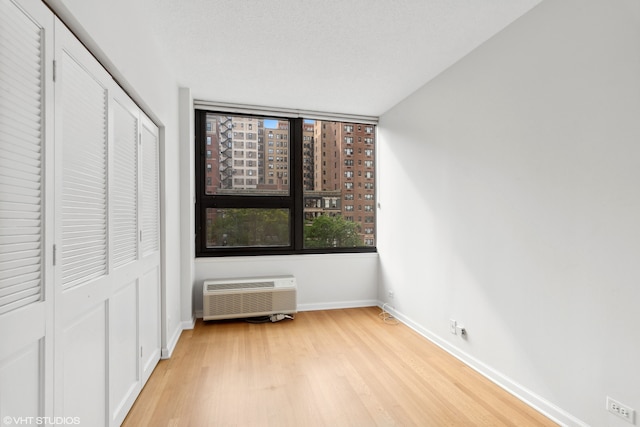 unfurnished bedroom featuring a textured ceiling, a closet, light wood-type flooring, and an AC wall unit