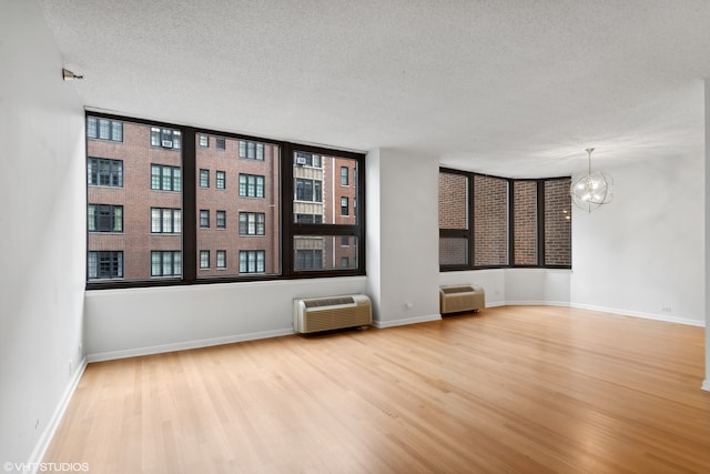 unfurnished room with wood-type flooring, a textured ceiling, a chandelier, and a wall mounted AC