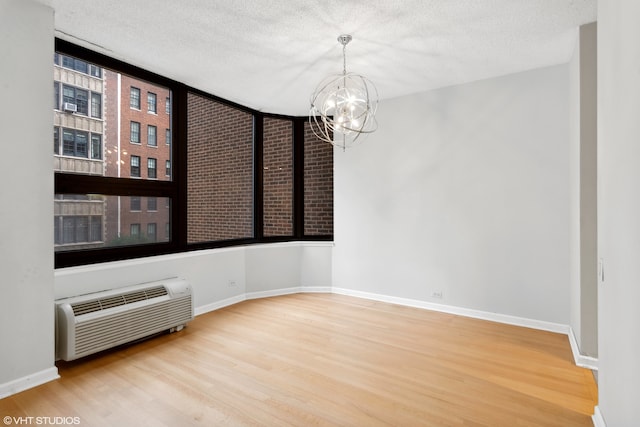 unfurnished room with wood-type flooring, a notable chandelier, a textured ceiling, and a wall mounted AC