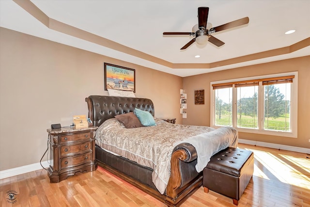 bedroom featuring ceiling fan, light wood-type flooring, and a raised ceiling