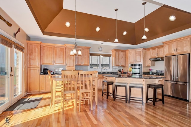 kitchen with light wood-type flooring, high end fridge, hanging light fixtures, and a raised ceiling