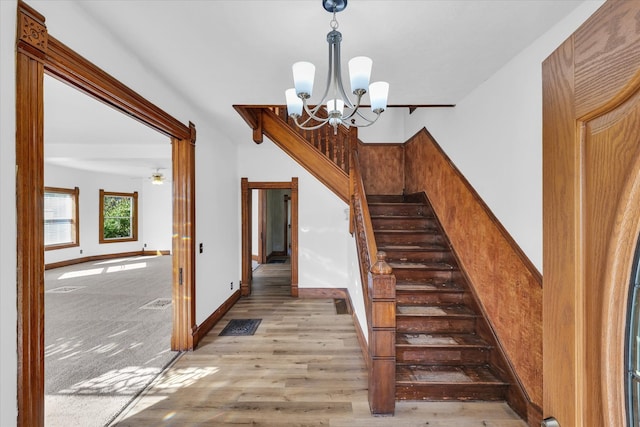 stairs featuring ceiling fan with notable chandelier and hardwood / wood-style flooring