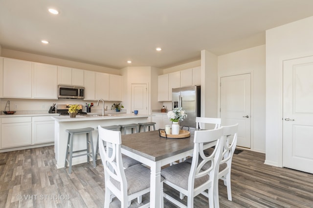 kitchen with stainless steel appliances, wood-type flooring, sink, an island with sink, and white cabinetry