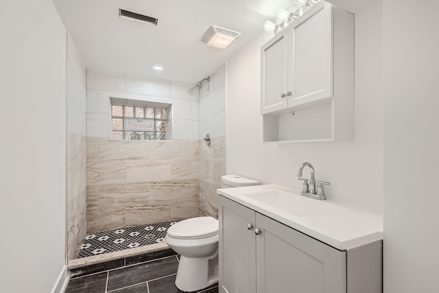 bathroom with vanity, toilet, and tiled shower