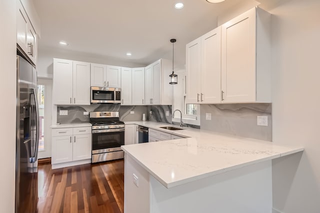 kitchen with white cabinetry, kitchen peninsula, stainless steel appliances, decorative light fixtures, and sink