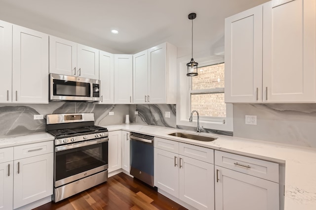 kitchen with pendant lighting, appliances with stainless steel finishes, sink, and white cabinets