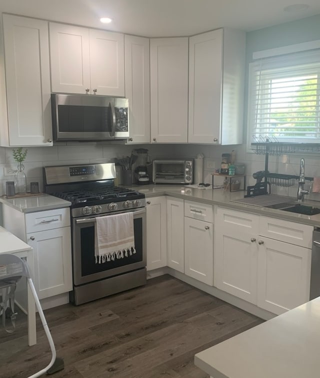 kitchen with dark wood-type flooring, decorative backsplash, white cabinetry, and stainless steel appliances