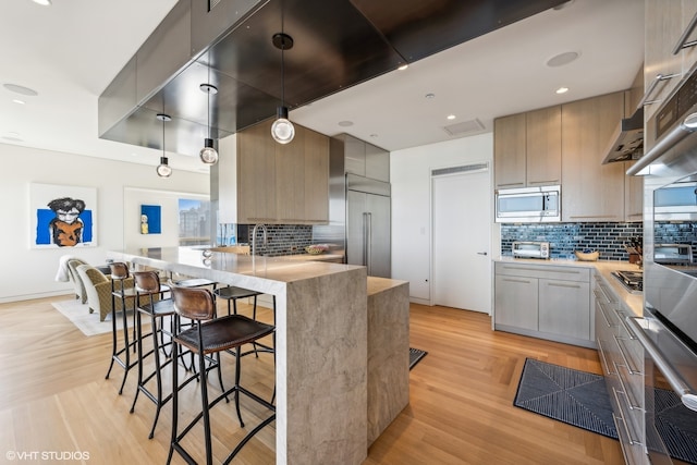 kitchen featuring tasteful backsplash, kitchen peninsula, a kitchen breakfast bar, built in appliances, and light hardwood / wood-style flooring