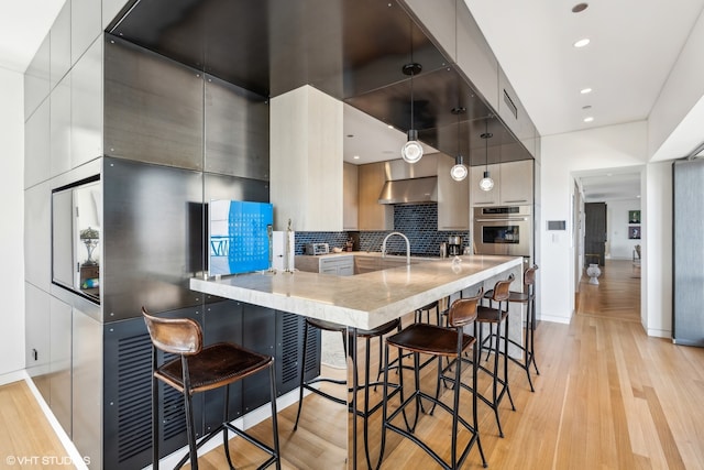 kitchen with oven, a kitchen bar, backsplash, kitchen peninsula, and light hardwood / wood-style floors