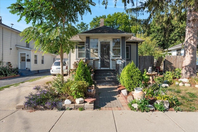 bungalow-style house featuring entry steps, fence, and a chimney