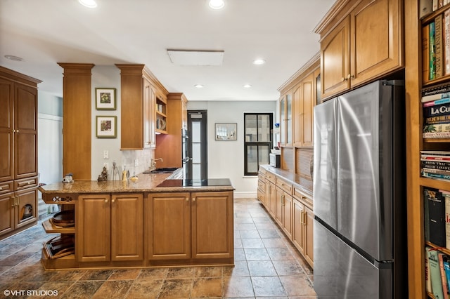 kitchen with kitchen peninsula, backsplash, stone counters, stainless steel refrigerator, and decorative columns