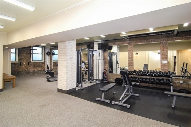 workout area featuring ornate columns and brick wall