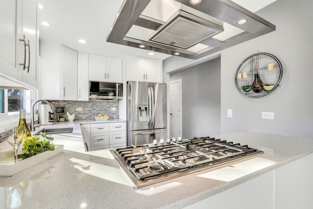 kitchen with tasteful backsplash, stainless steel appliances, sink, white cabinetry, and range hood