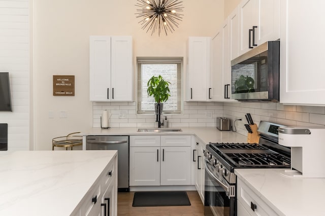 kitchen featuring light stone counters, sink, white cabinetry, stainless steel appliances, and decorative backsplash