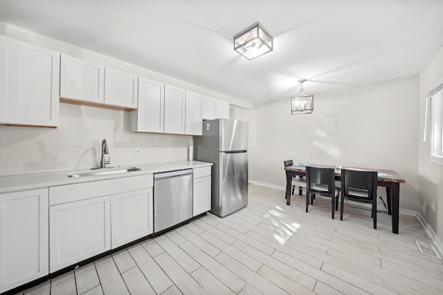 kitchen with white cabinets, stainless steel appliances, sink, and decorative light fixtures