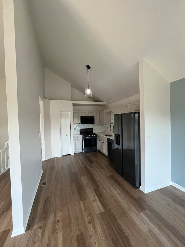 kitchen featuring dark wood-type flooring, lofted ceiling, hanging light fixtures, black appliances, and backsplash