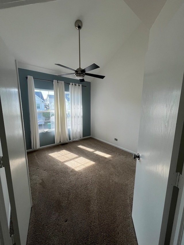 empty room featuring dark carpet, vaulted ceiling, and ceiling fan