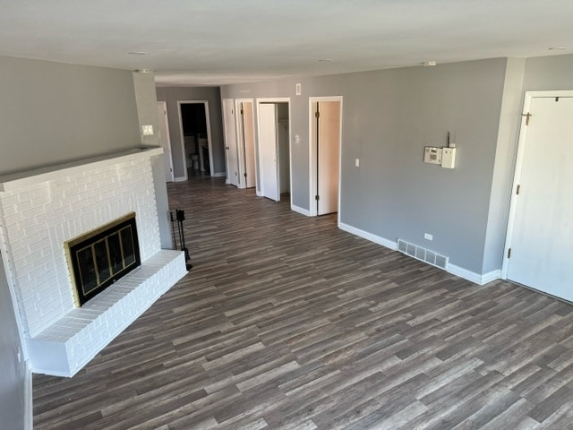 unfurnished living room with a brick fireplace and dark hardwood / wood-style floors