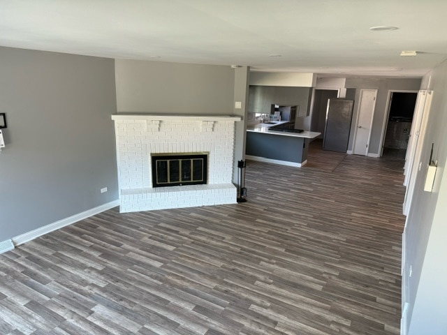 unfurnished living room featuring a brick fireplace and dark hardwood / wood-style floors