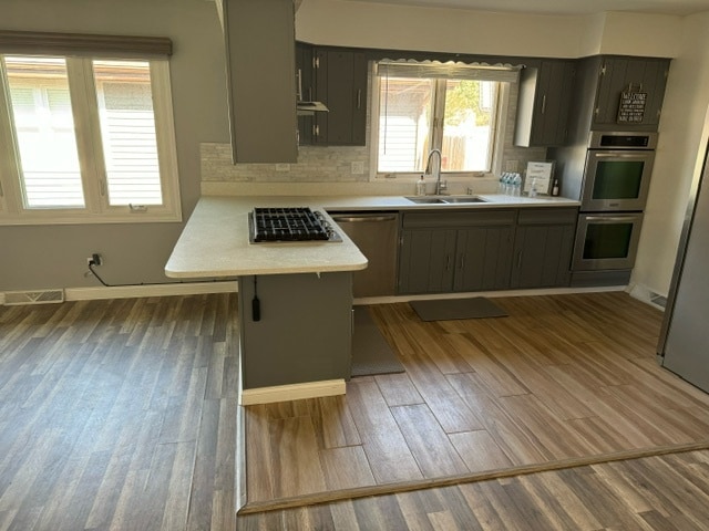 kitchen featuring appliances with stainless steel finishes, sink, light wood-type flooring, backsplash, and kitchen peninsula