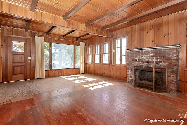 unfurnished living room featuring beamed ceiling, wood ceiling, a brick fireplace, wooden walls, and hardwood / wood-style floors