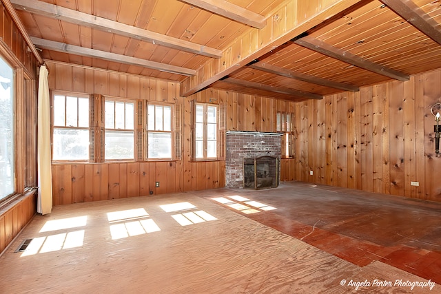 unfurnished living room featuring a fireplace, wood walls, beam ceiling, and wooden ceiling