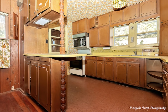 kitchen featuring wood walls, wall oven, oven, sink, and kitchen peninsula