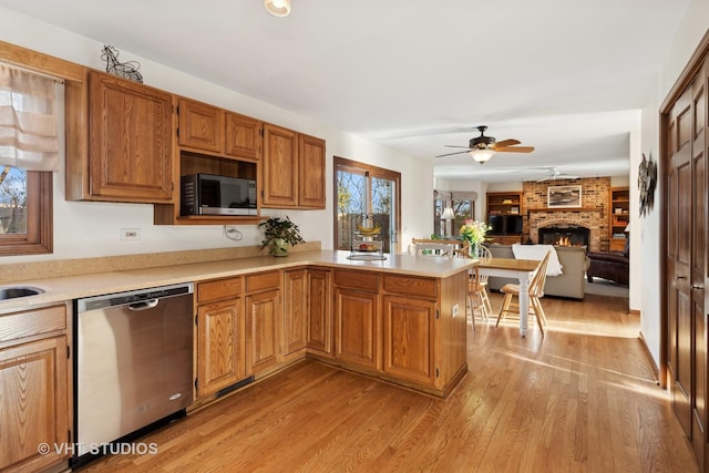 kitchen featuring dishwasher, ceiling fan, light hardwood / wood-style floors, a brick fireplace, and kitchen peninsula