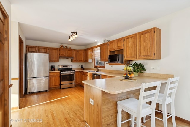 kitchen with sink, a breakfast bar area, stainless steel appliances, light hardwood / wood-style floors, and kitchen peninsula