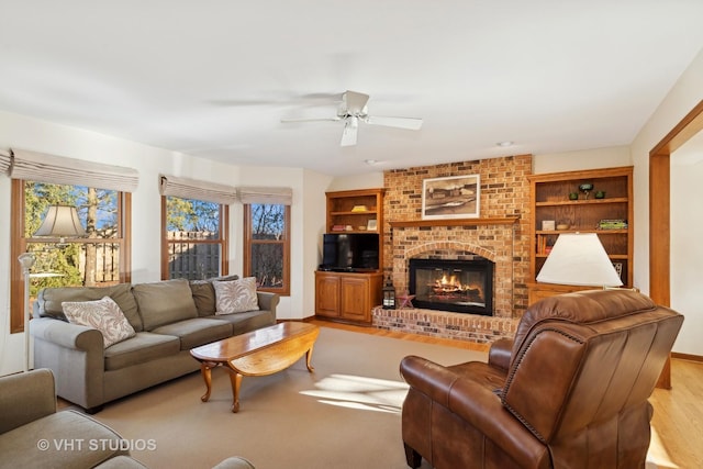 living room featuring ceiling fan, a brick fireplace, light wood-type flooring, and built in shelves