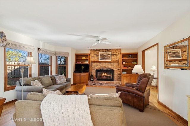 living room with a brick fireplace, ceiling fan, and built in shelves