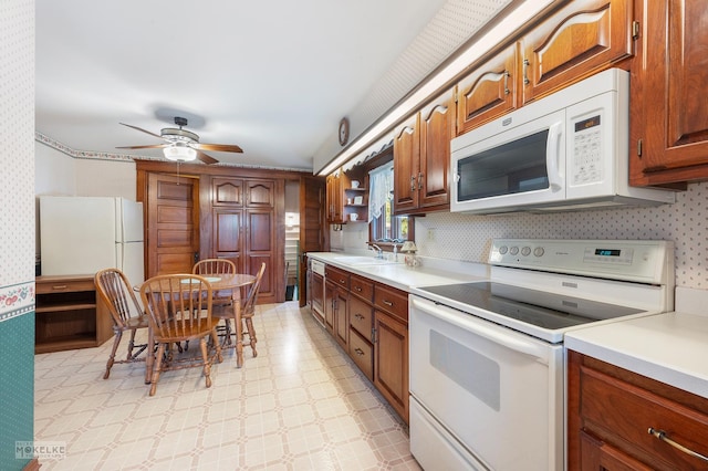 kitchen featuring wallpapered walls, white appliances, light countertops, a ceiling fan, and a sink