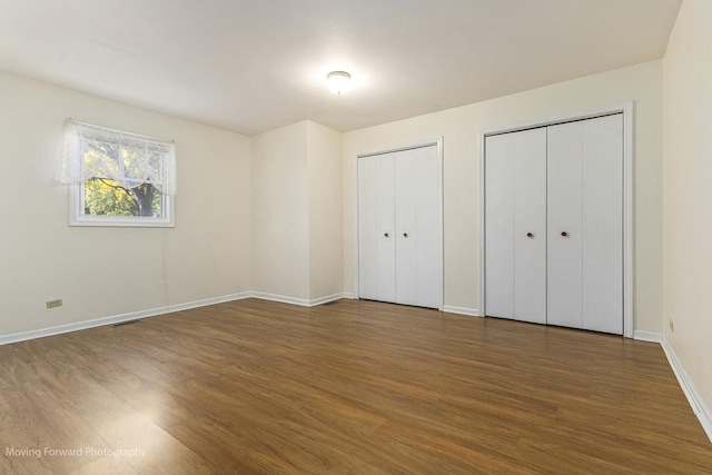 unfurnished bedroom with multiple closets and dark hardwood / wood-style flooring