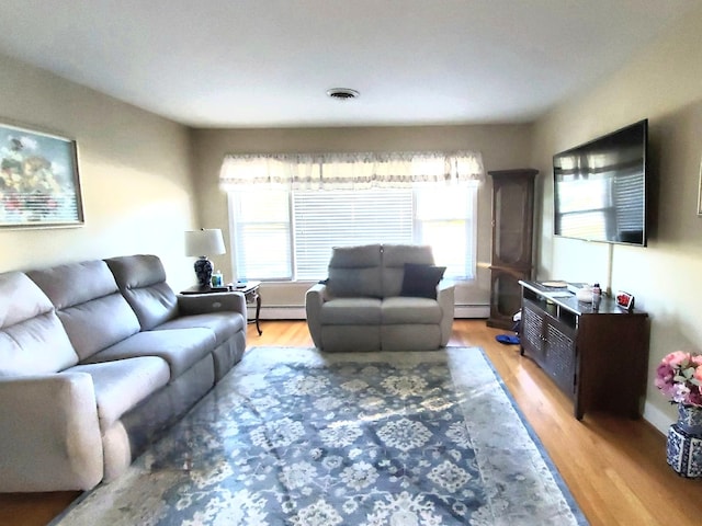 living room featuring light wood-type flooring, a baseboard heating unit, and a wealth of natural light