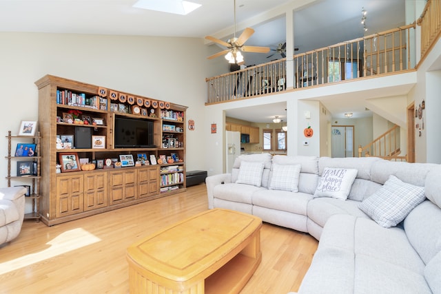 living room with high vaulted ceiling, ceiling fan, hardwood / wood-style flooring, a skylight, and beam ceiling