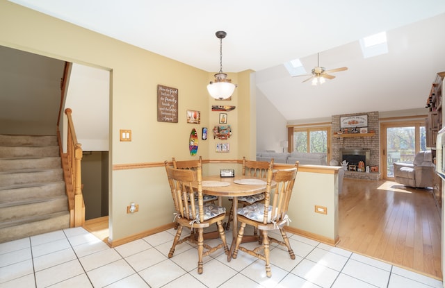 dining area featuring a fireplace, ceiling fan, vaulted ceiling with skylight, and light hardwood / wood-style flooring