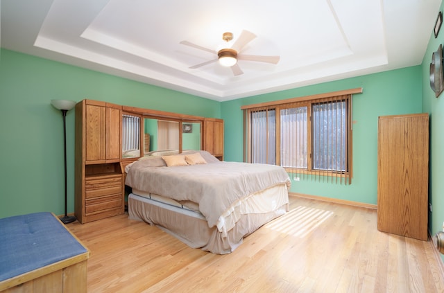 bedroom with ceiling fan, a raised ceiling, and light wood-type flooring