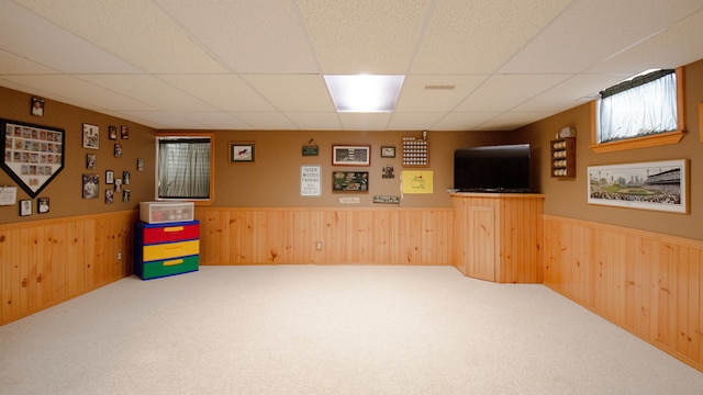 basement with carpet flooring, a paneled ceiling, and wood walls