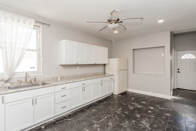 kitchen featuring ceiling fan, sink, white cabinetry, light stone countertops, and white fridge