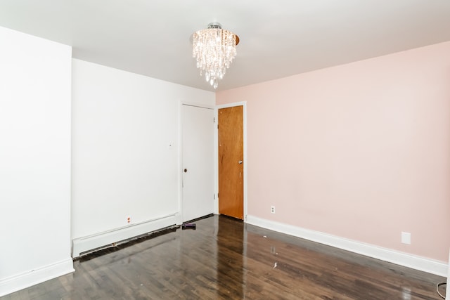 spare room with dark wood-type flooring, an inviting chandelier, and baseboard heating